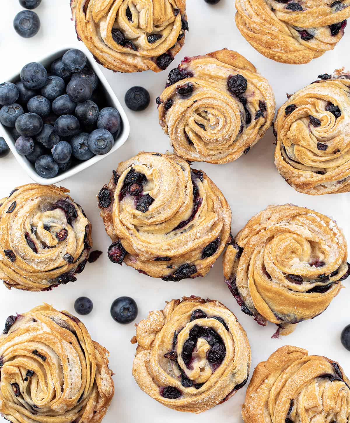 Blueberry Cruffins will be your new favorite blueberry treat! They are made with fresh blueberries rolled into crescent roll sheets and then baked. It's layer after layer of soft dough bursting with blueberries in every bite! Blueberry Cruffins From Overhead on a White Counter with Fresh Blueberries.