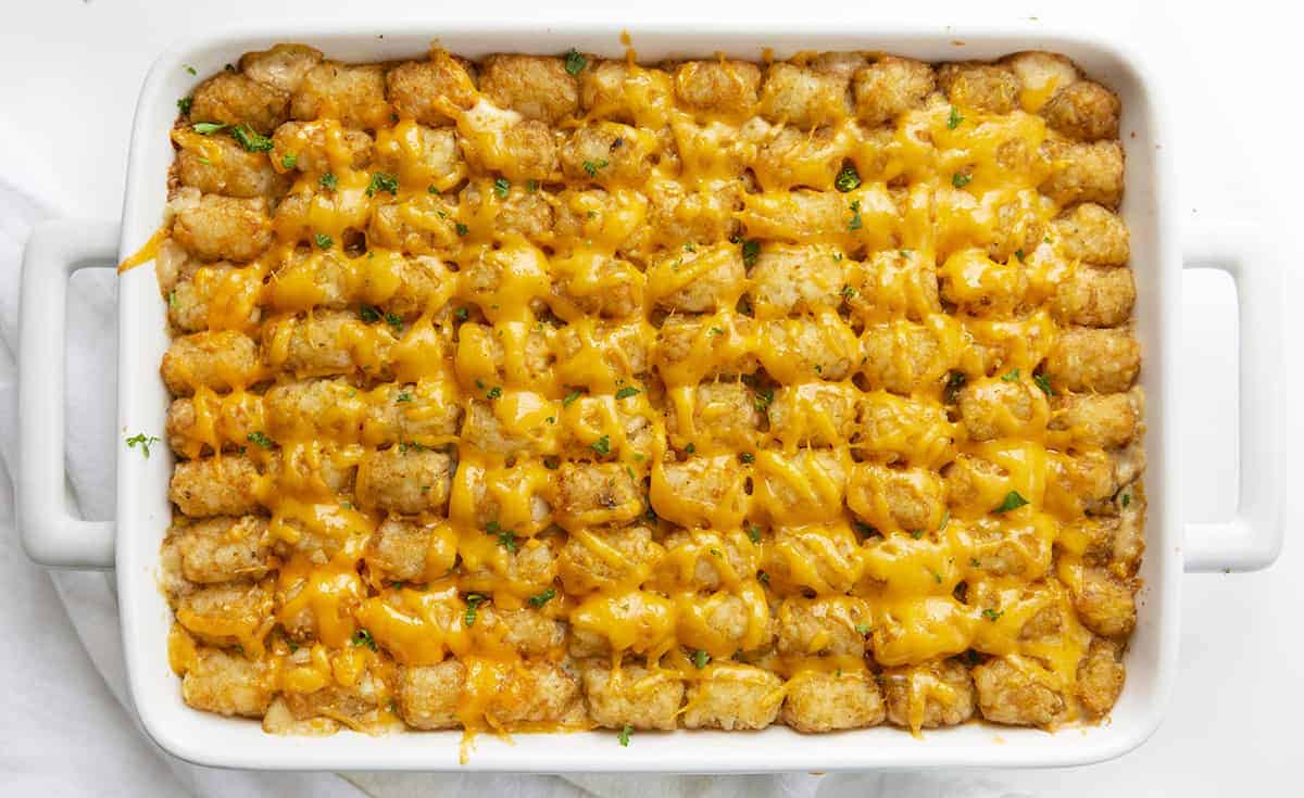 Tater Tot Hotdish is a quick and easy comfort food staple recipe all over the Midwest! This hotdish is full of meat, veggies, soup, cheese, and topped with tater tots for a super satisfying meal! Tater Tot Hotdish, Tater Tot Casserole, How to Make Hotdish, Casserole, Tater Tot Recipes, Dinner, Supper, Recipes, Dinner Ideas, Midwest Recipes, i am baker, iambaker Overhead of Tater Tot Hotdish in White Casserole Pan with White Towel
